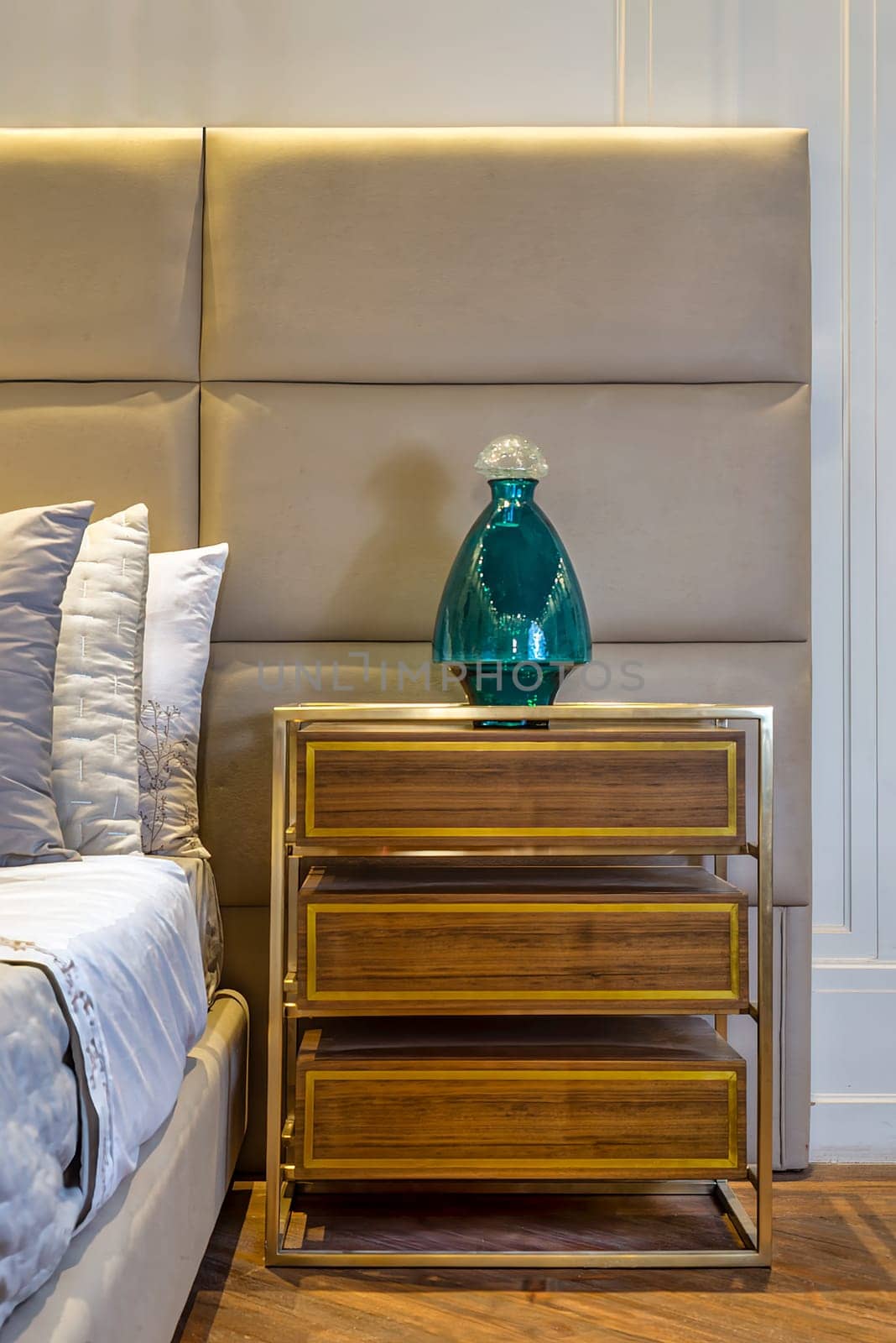 A bedroom with hardwood flooring, featuring a wooden bed and a nightstand made of cabinetry. The nightstand has a vase on top, adding a natural touch to the room