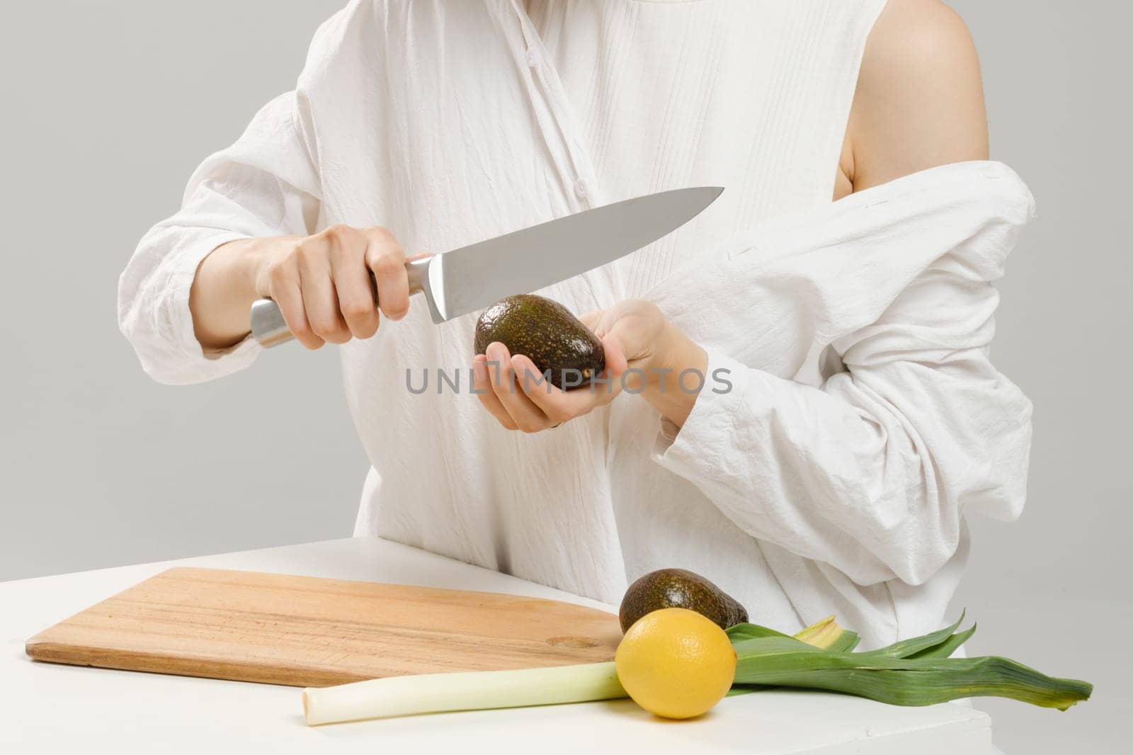 Unrecognizable woman cutting fresh avocado into halves. Concept of balanced eating.