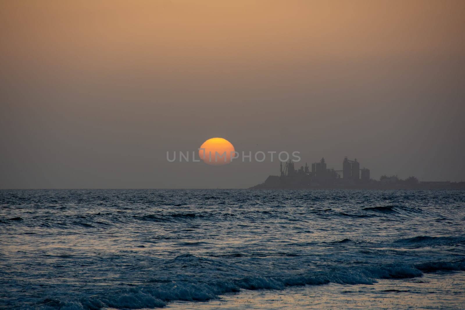 Sunset over the sea with a city in silhouette in the background