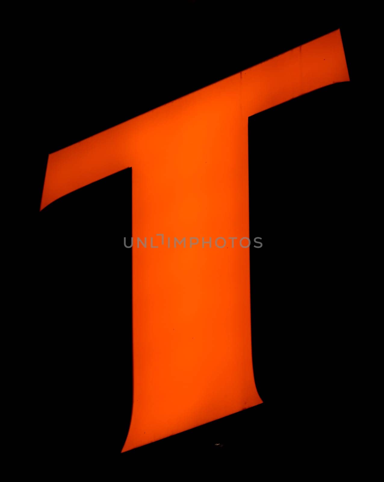 Captured from below is a striking, luminous 'T' set against a dark backdrop. Its audacious orange hue stands out vividly, contrasting sharply with its surroundings. Such a design choice might signify