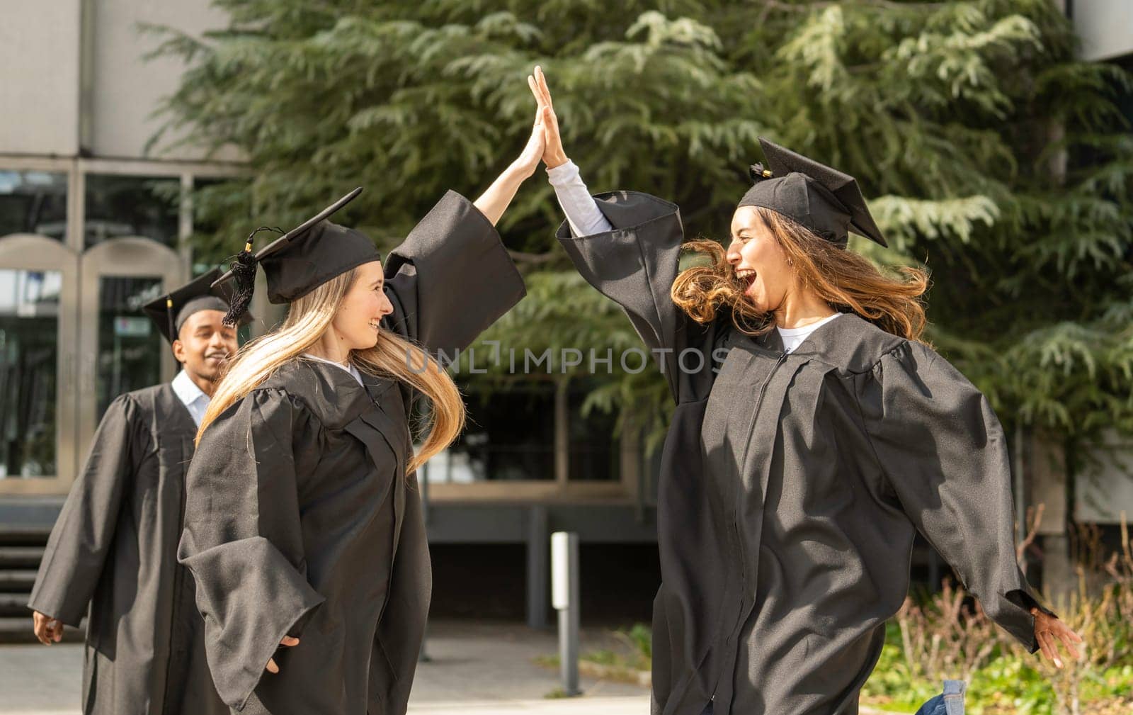 Two excited female graduates giving high five to each other, celebrating successful graduation