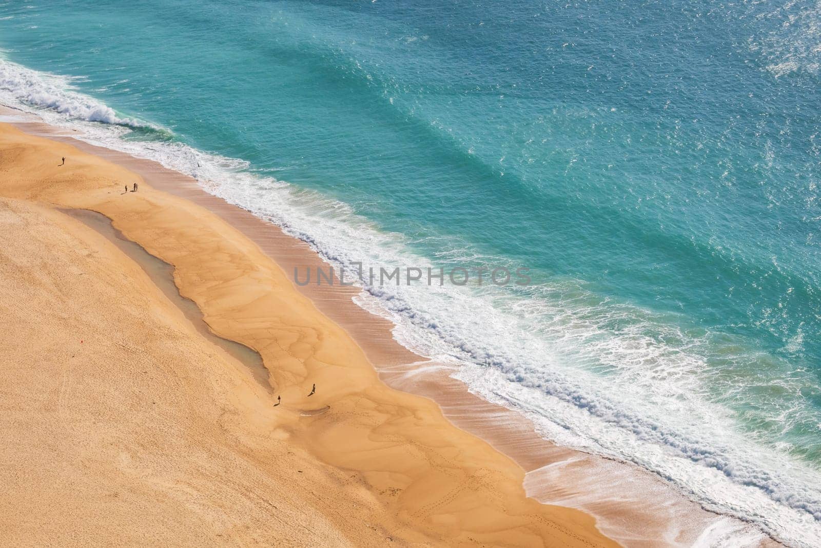 Aerial view of the sandy beach and the turquoise waves of the Atlantic ocean in Nazaré, Portugal