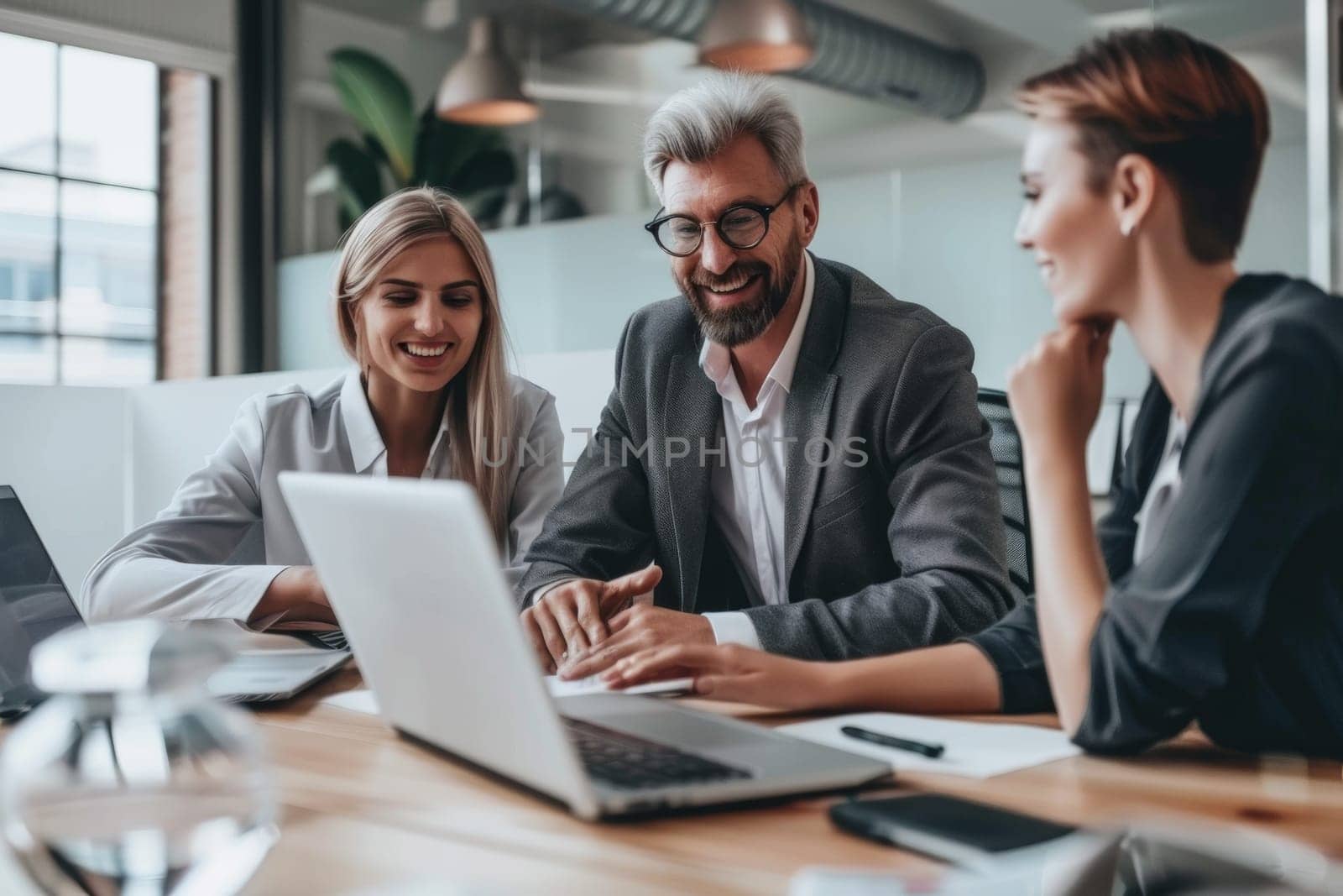 Business professionals smiling while discussing work at a contemporary office desk with a laptop