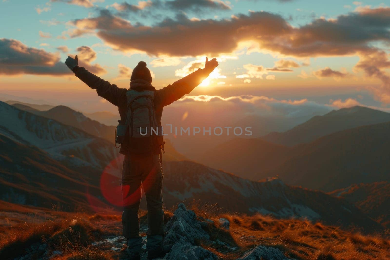 Man celebrating with arms raised at the summit during a stunning sunset landscape