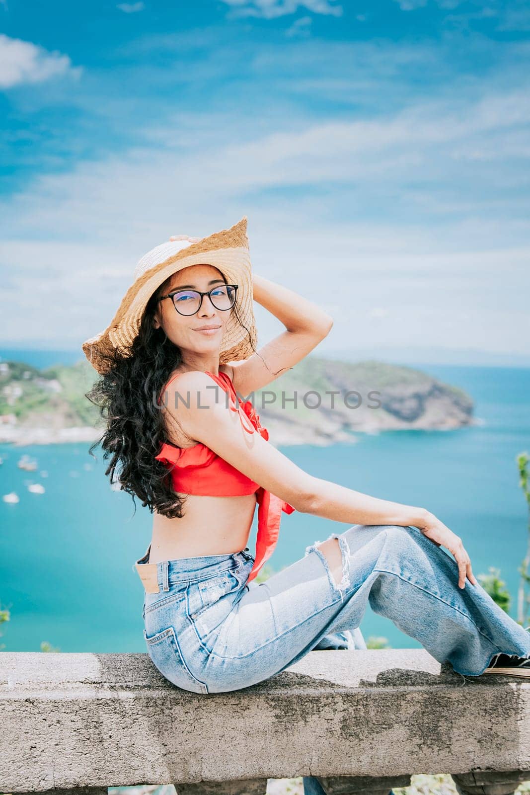 Beautiful tourist girl in a viewpoint with a beach in the background. Happy tourist sitting at a viewpoint looking at the camera with bay in the background
