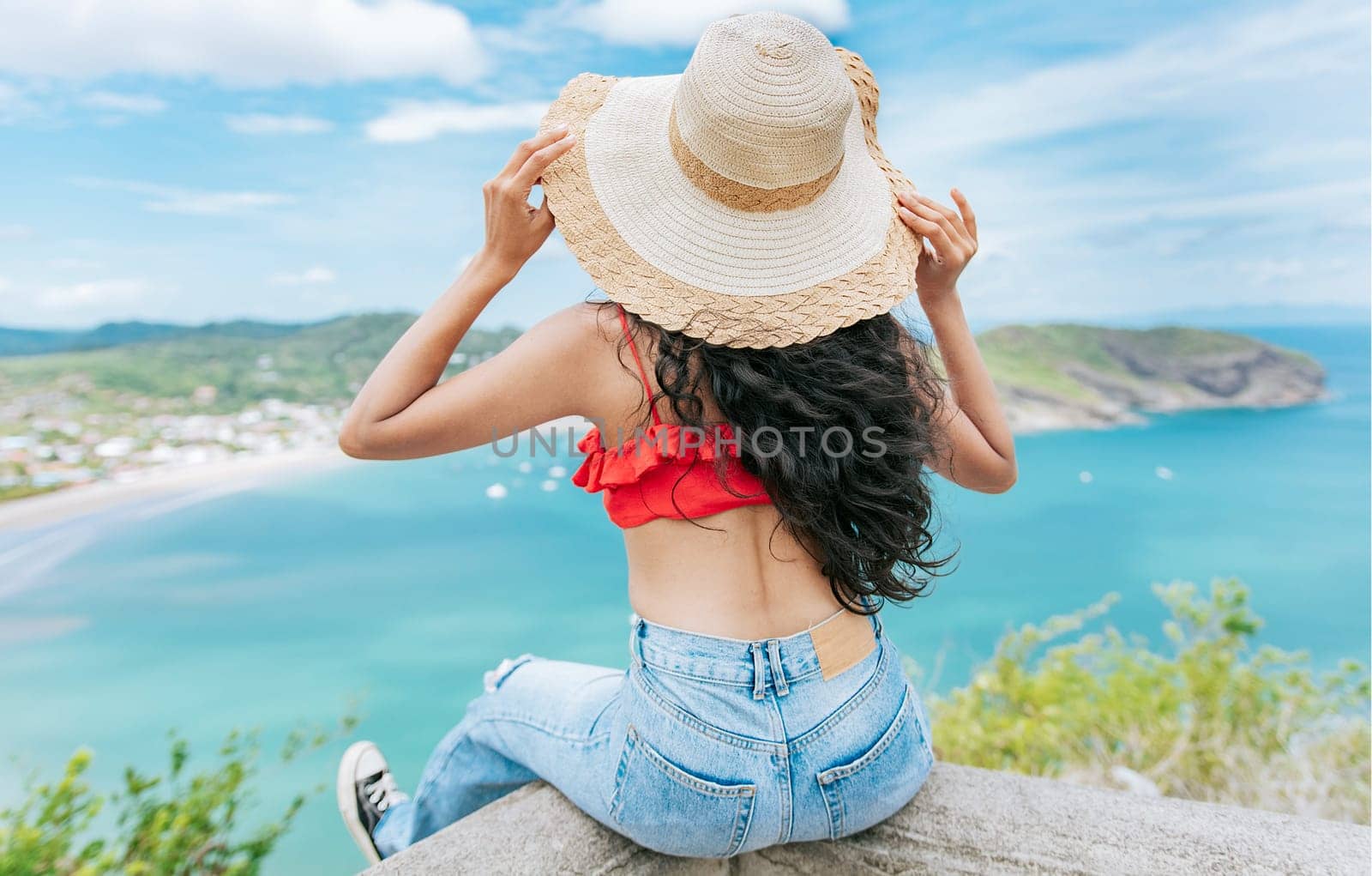Rear view tourist girl sitting at a viewpoint looking at the beach. Back view of woman on vacation looking at the beach at a viewpoint