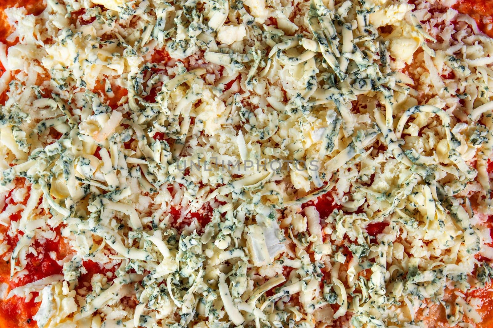 A tantalizing close-up view of a pizza prepared for the oven, showcasing its delicious toppings of tomato sauce, grated cheese, and finely chopped basil. With no visible crust, this pizza promises a mouthwatering experience.