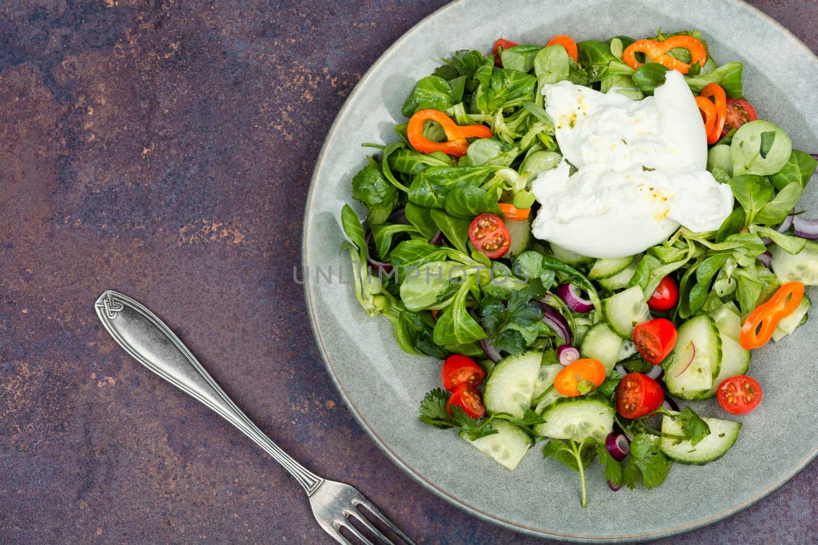 Heathy salad of leafy greens, cherry tomatoes, cucumbers, peppers and Burrata cheese. Close up.