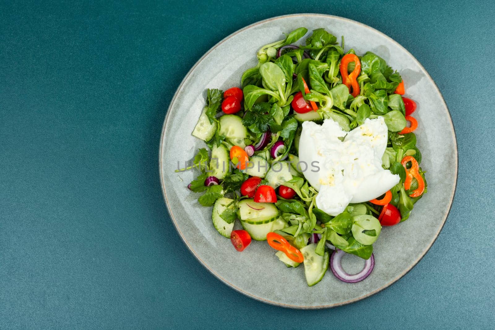 Heathy salad of leafy greens, cherry tomatoes, cucumbers, peppers and Burrata cheese. Close up.