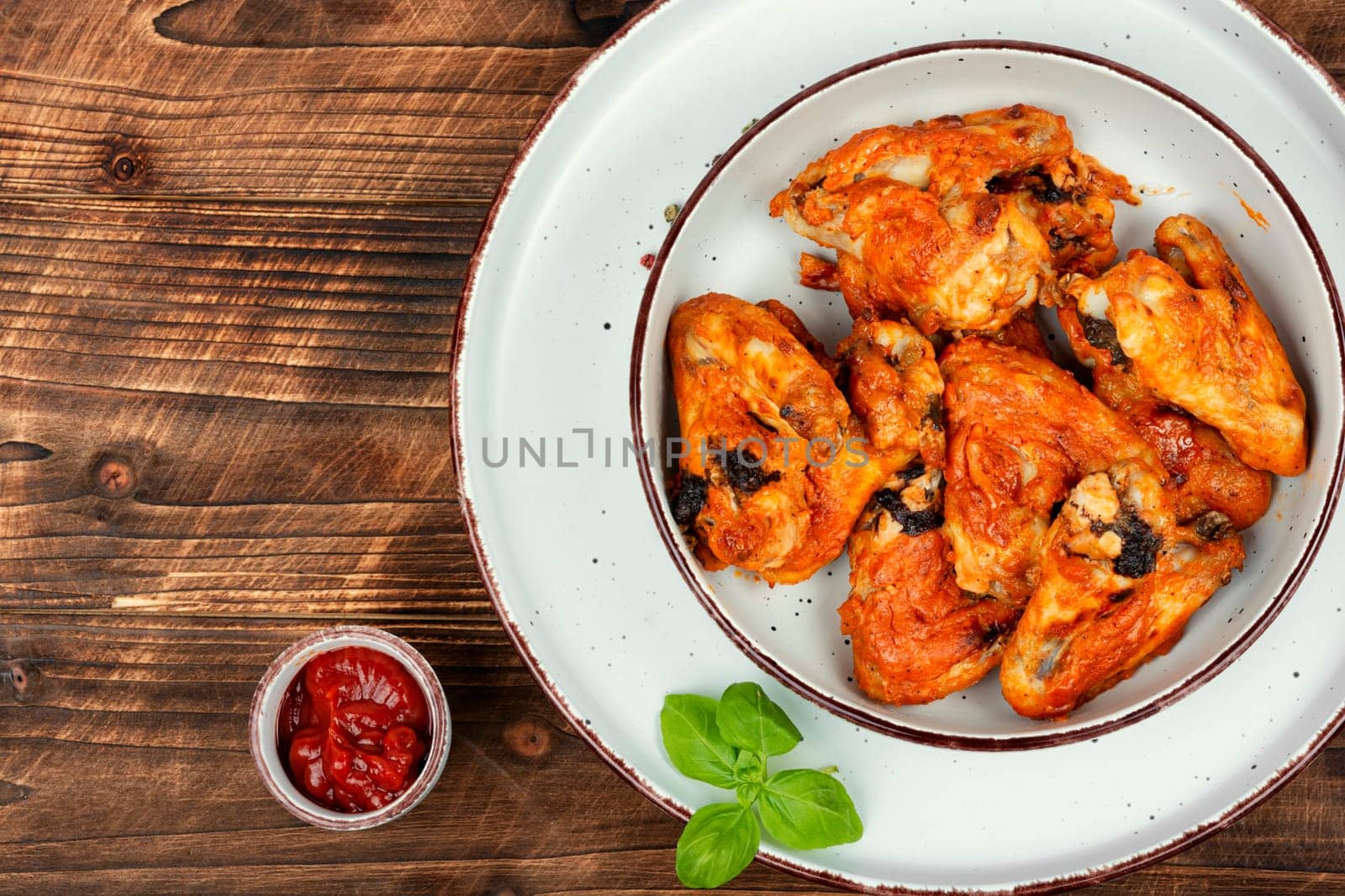 Baked chicken wings with chili sauce on rustic wooden table. Space for text.