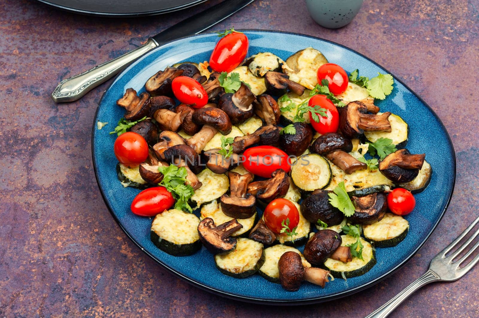 Mushrooms, zucchini and tomatoes baked in the oven on rustic wooden table. Copy space.