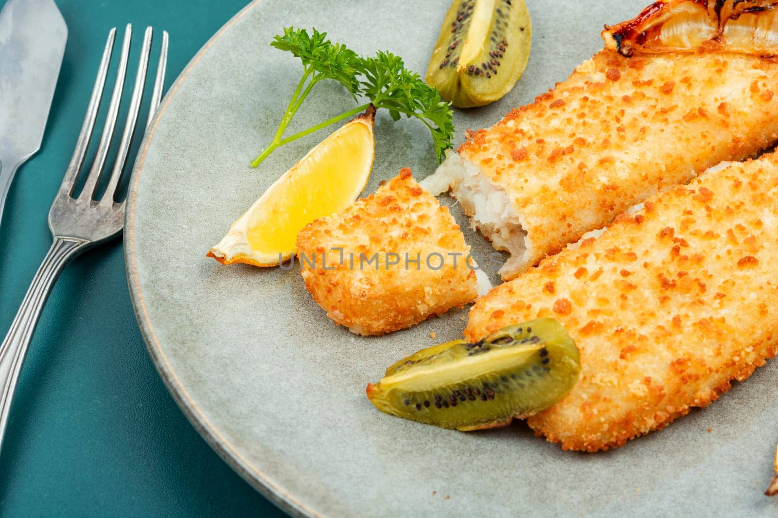 Pollock fillet roasted in bread crumbs served with sauce and kiwi. Fish in chips.
