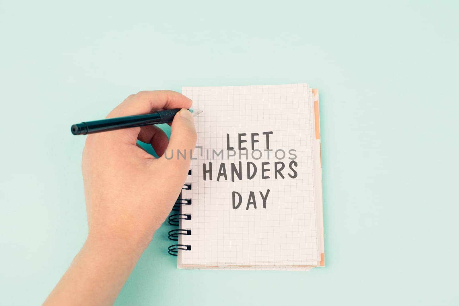 Left handers day is standing on a notebook, writing with the left hand, pen and table