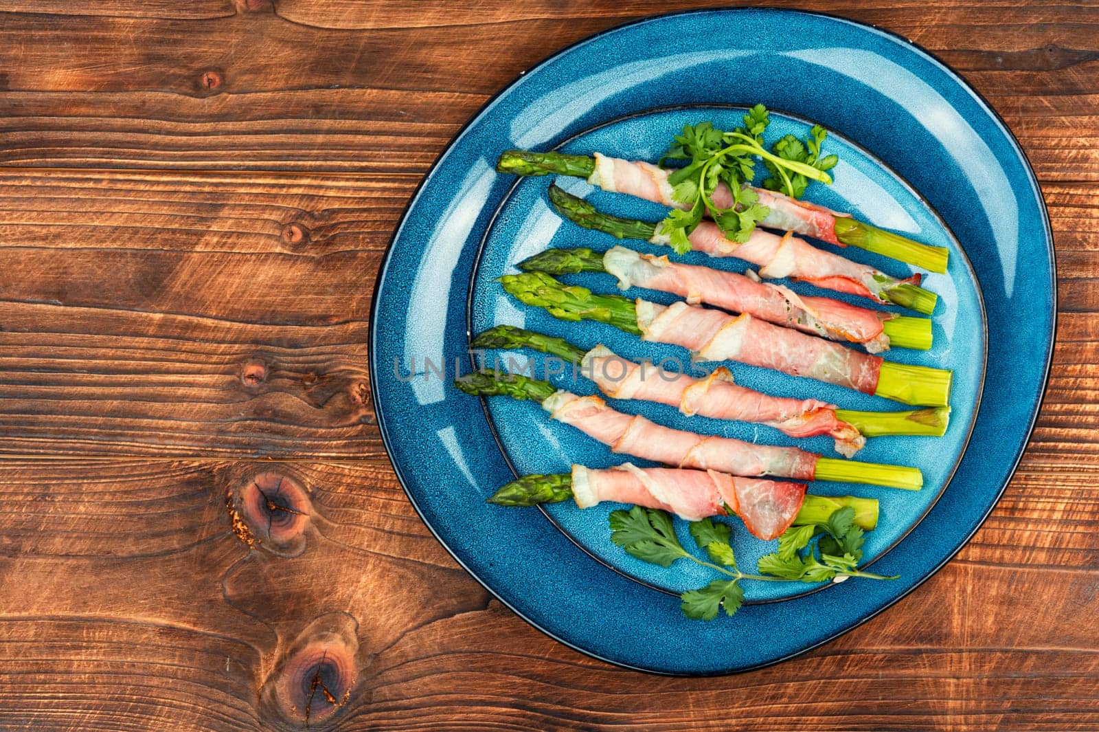 Green asparagus baked in bacon on a wooden background, rustic style. Space for text