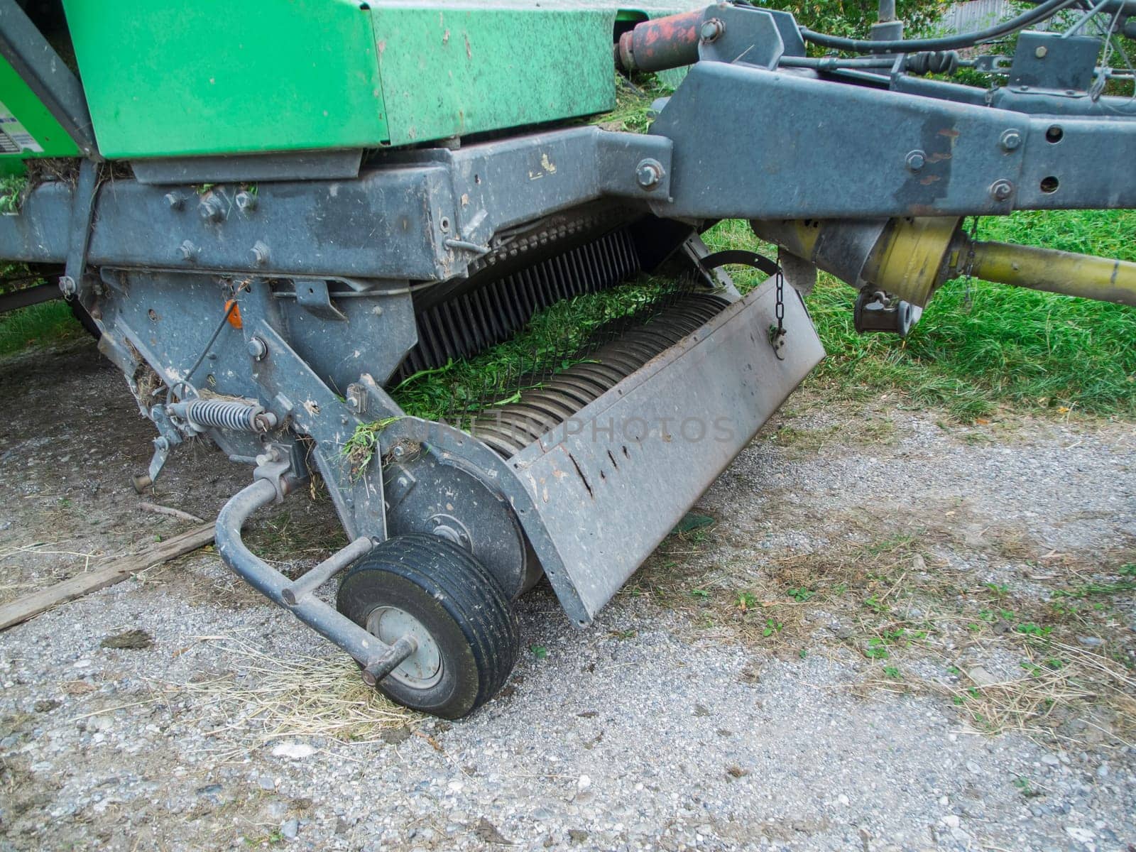 Partial view of the PTO spring tines and pickup roller of a baler on a gravel surface after intensive use.