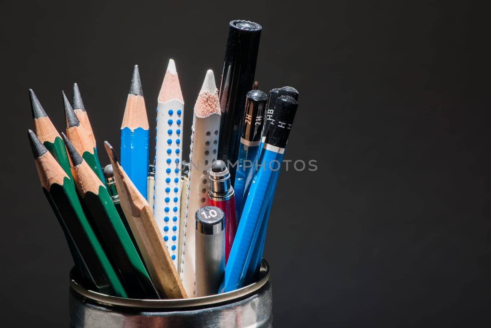 Small assortment of pencils standing vertically in a tin can against a dark background.