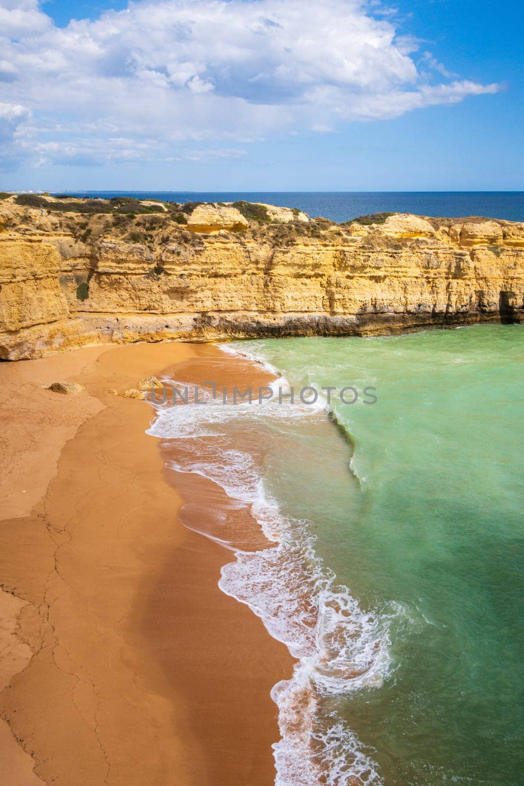 Vertical view of cliffs and ocean waves crashing onto Praia da Ponta Pequena beach near Albufeira, Algarve, Portugal