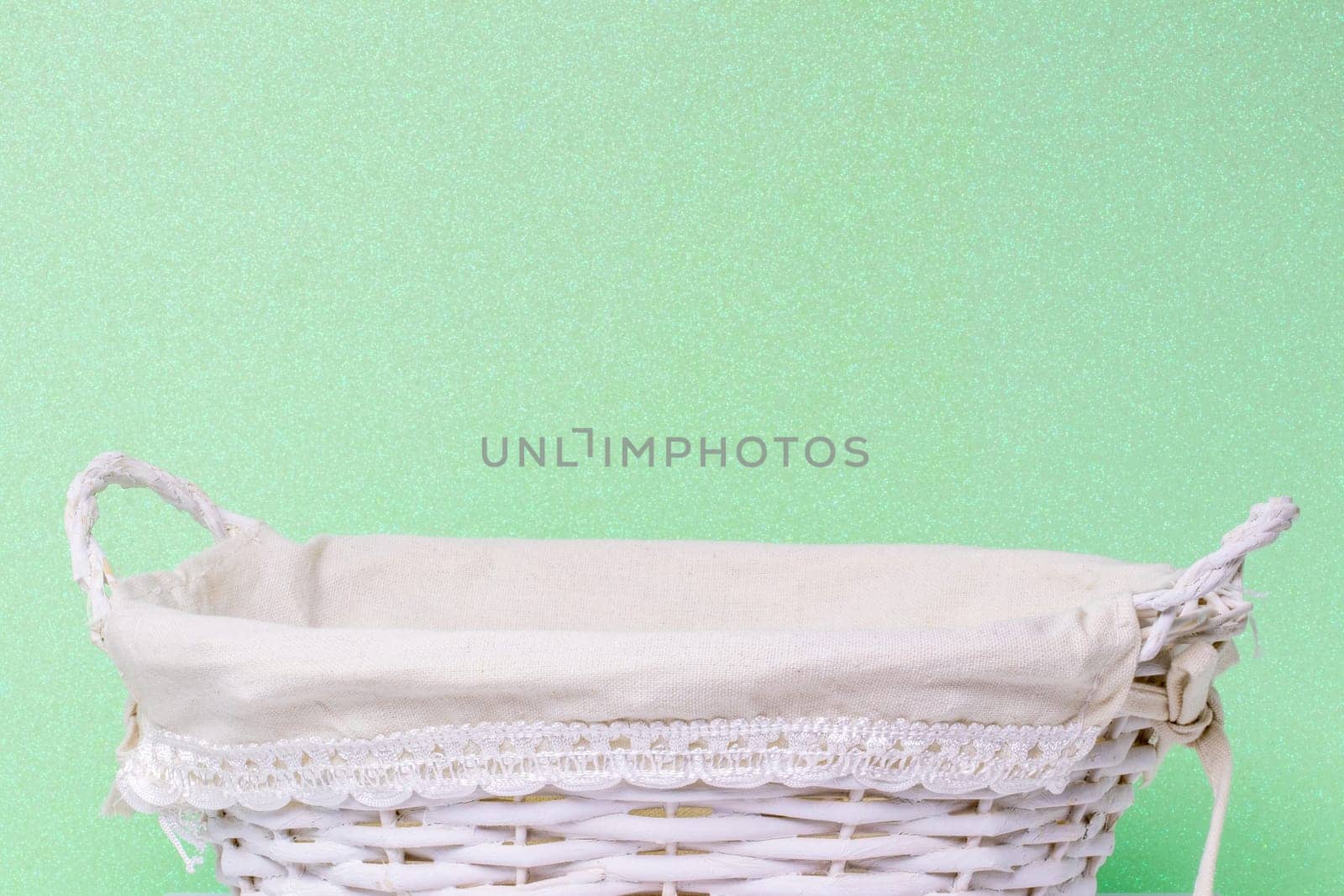 Empty wicker basket over light green glittering background. For your food and product display assembly. Macro of a straw basket.