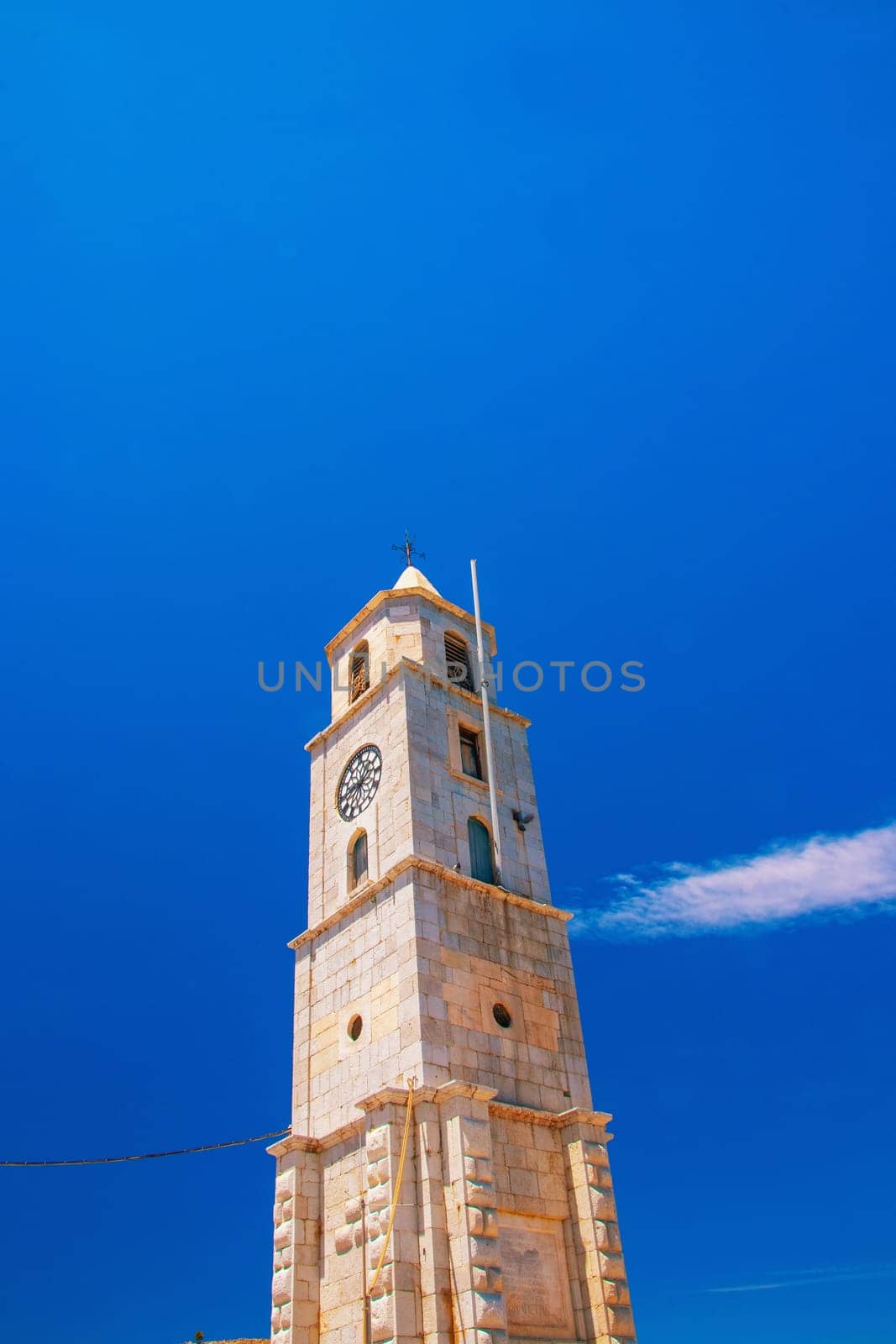 SYMI, Greece - 03 June 2021 The top of the imposing clock tower (Roloi), which stands right at the entrance to the port of Symi. Next to it the police station building.
