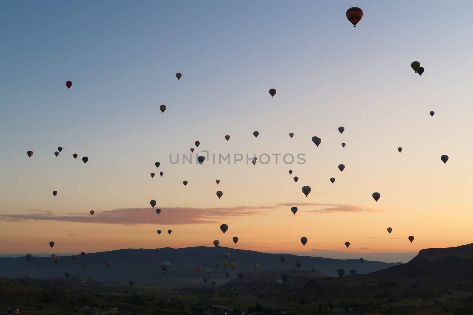 Dozens of hot air balloons rising over the landscape of the Red Valley, Rose Valley before sunrise, close to Goreme, Cavusin, Cappadocia, Turkey 2022