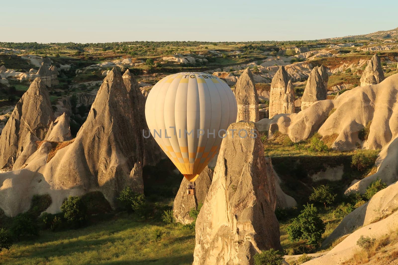 Yellow and white hot air balloon maneuvering between the fairy chimneys of Cappadocia, close to Göreme, Cappadocia, Turkey 2022