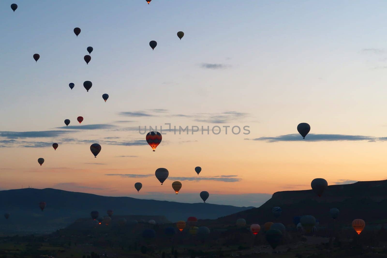 Many hot air balloons rising over the landscape of the Red Valley, Rose Valley before sunrise, close to Goreme, Cavusin, Cappadocia, Turkey 2022