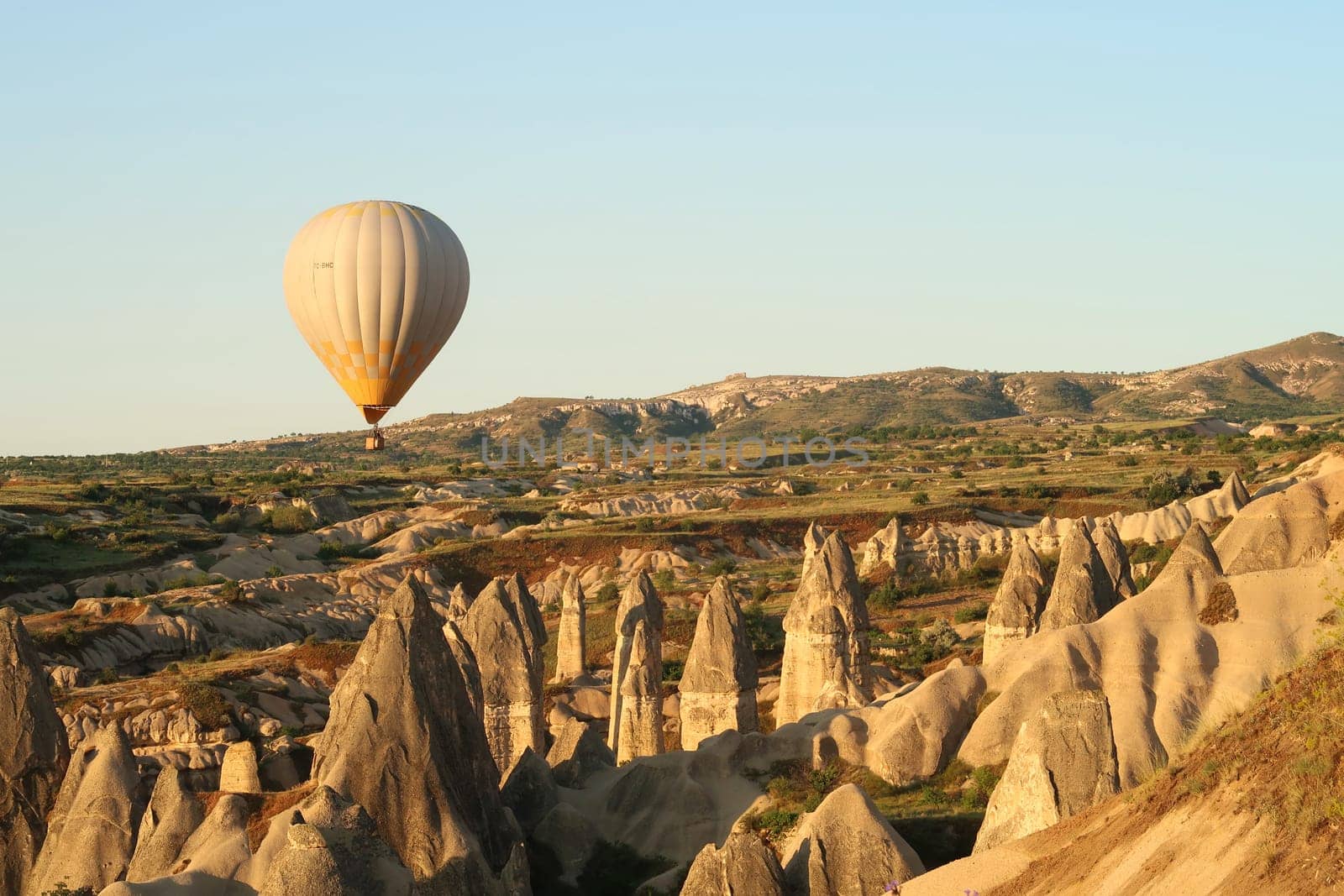 Yellow and white hot air balloon flying over the landscape of Cappadocia with its famous fairy chimneys, close to Göreme, Cappadocia, Turkey 2022