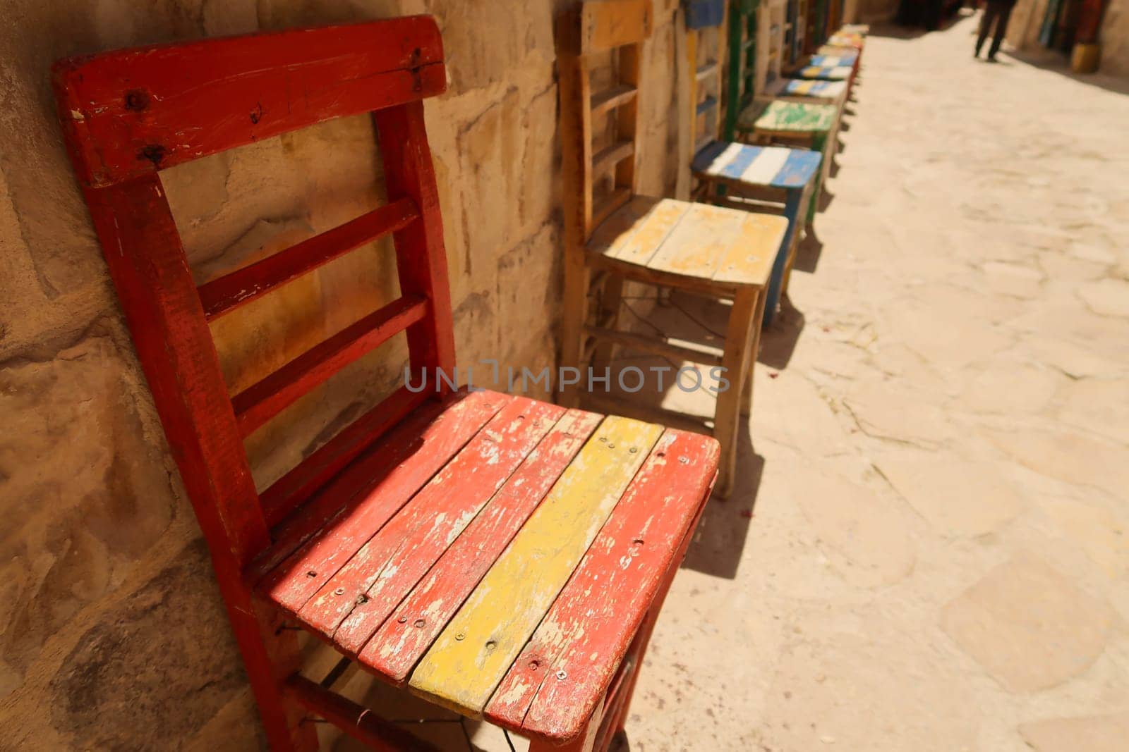 A row of colorful wooden chairs in a row in front of a wall in the old town of Mardin, Turkey 2022