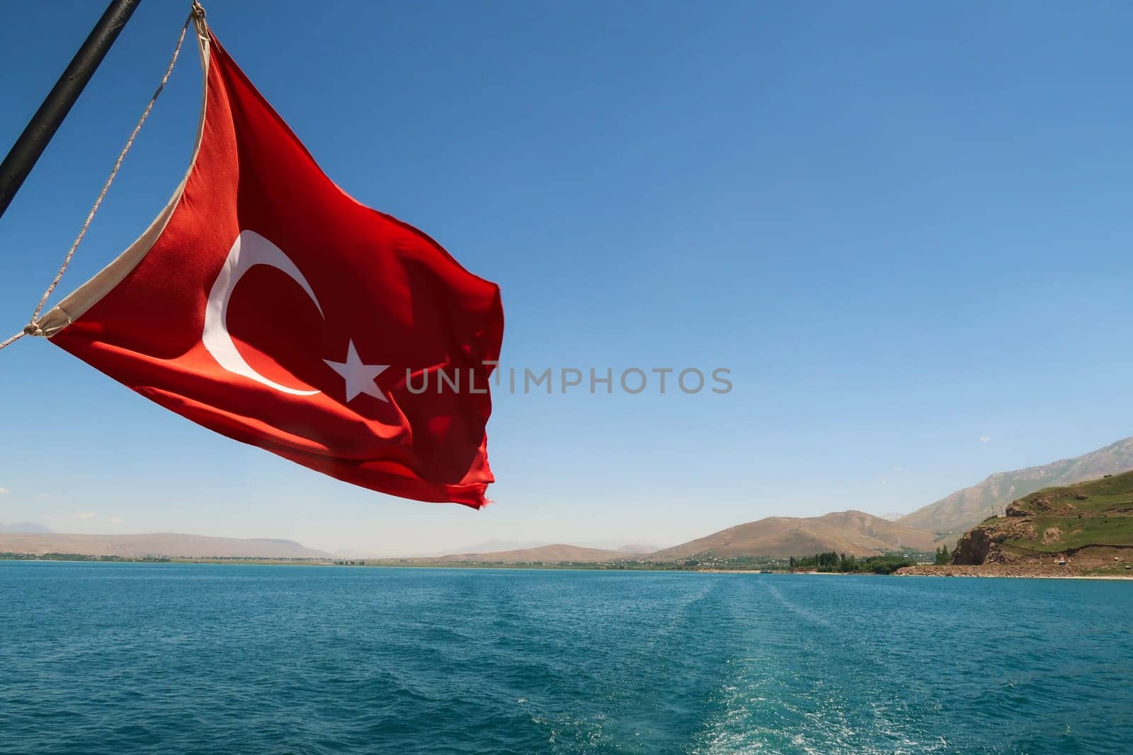 Red national flag of turkey flying, waving in the wind on the boat ride crossing Lake Van, Van Gölü to Akdamar Island, close to Van, Turkey 2022