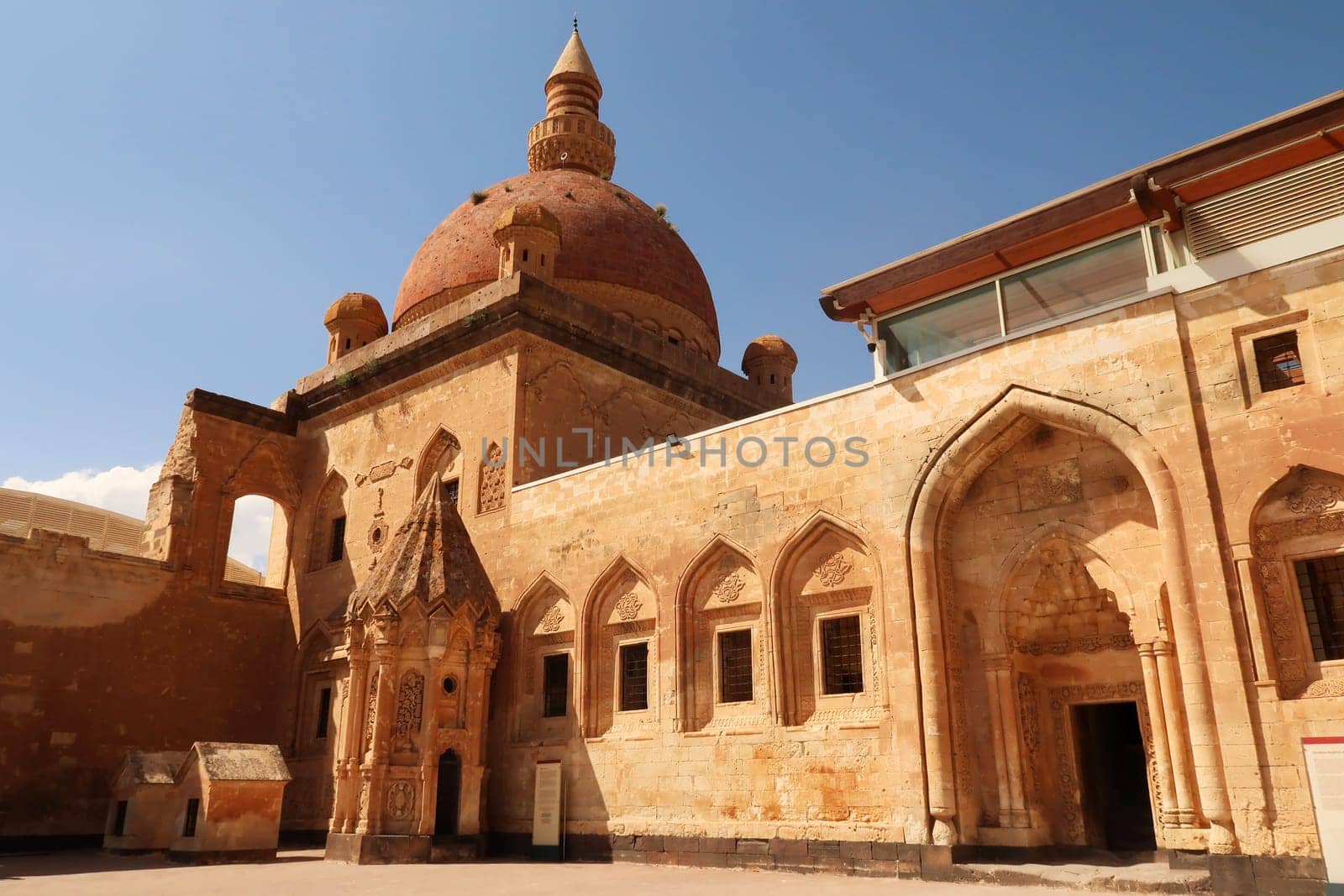 Ottoman tomb next to a row of barred windows and a gate with the mosque with its red cupola, dome in the background, in the second court inside the Ishak Pasha Palace, Sarayi, Dogubeyazit, Turkey 2022