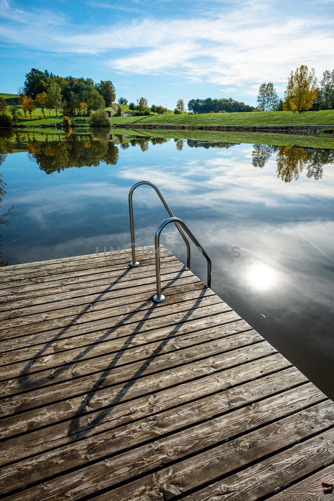 Dock at a lake with back lit sun and green meadow scenery