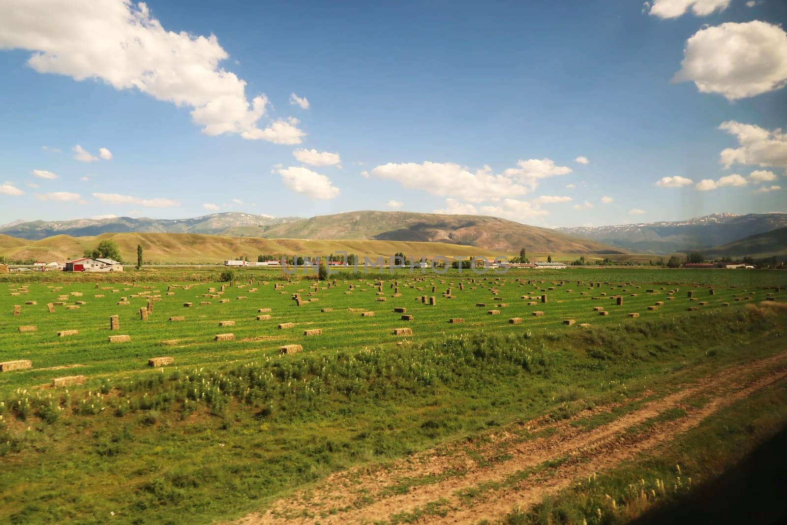 Passing farming, agriculture on the train ride in the Eastern Express, Dogu Ekspresi from Kars to Ankara, green field with hay bales on it, Turkey 2022
