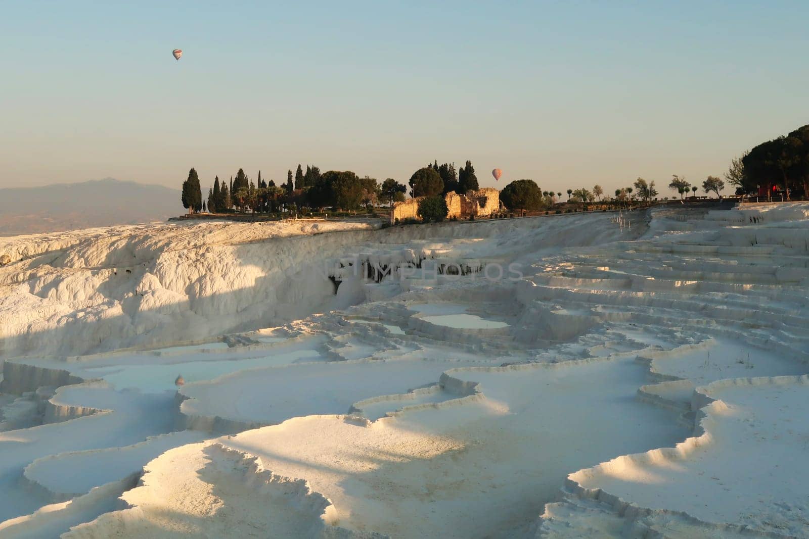The travertines of Pamukkale early in the morning with hot air balloons rising in the back, Denizli, Turkey 2022