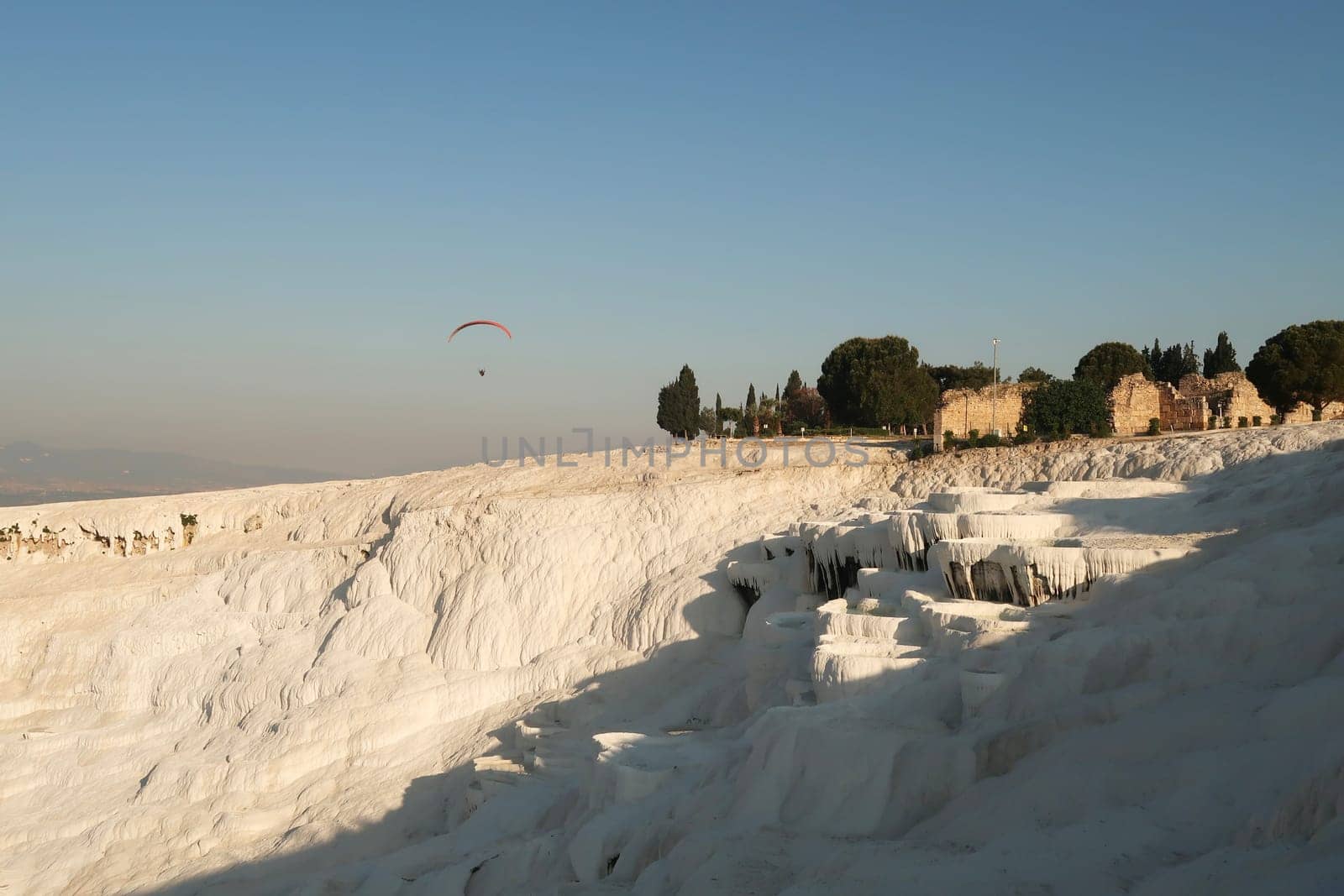 The impressive travertine terraces at Pamukkale in the early morning with a Paraglider in the background, Denizli, Turkey 2022
