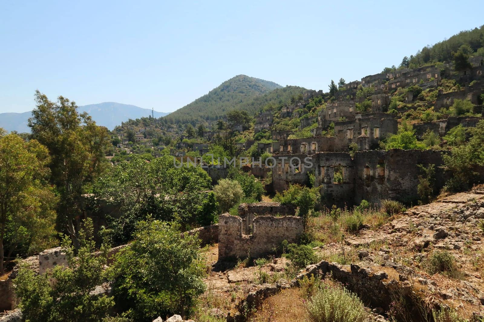 Cobble stone path leading up the hill with the ruins of the abandoned houses of Kayaköy in the background, near Fethiye, Turkey 2022