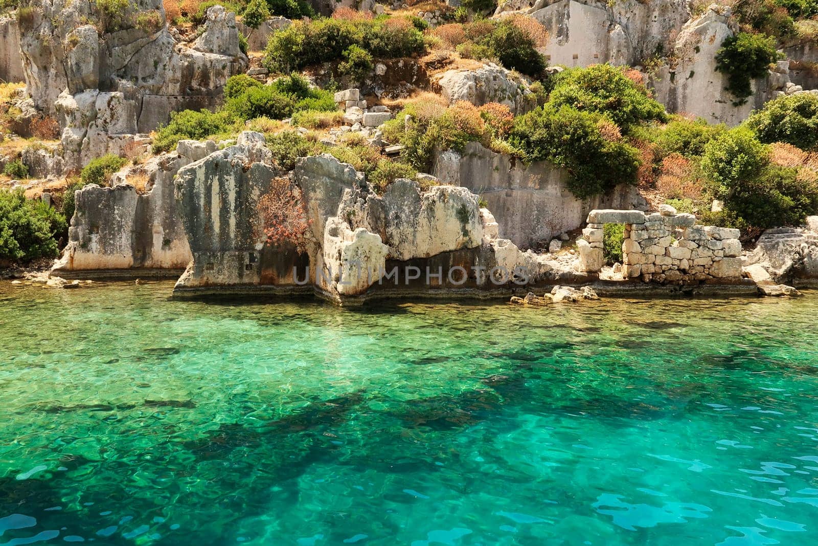 Submerged structures in the foreground, ruins of buildings, remaining wall with door in the background at the ancient sunken city of Kekova, Kekova Island, Demre, Turkey 2022