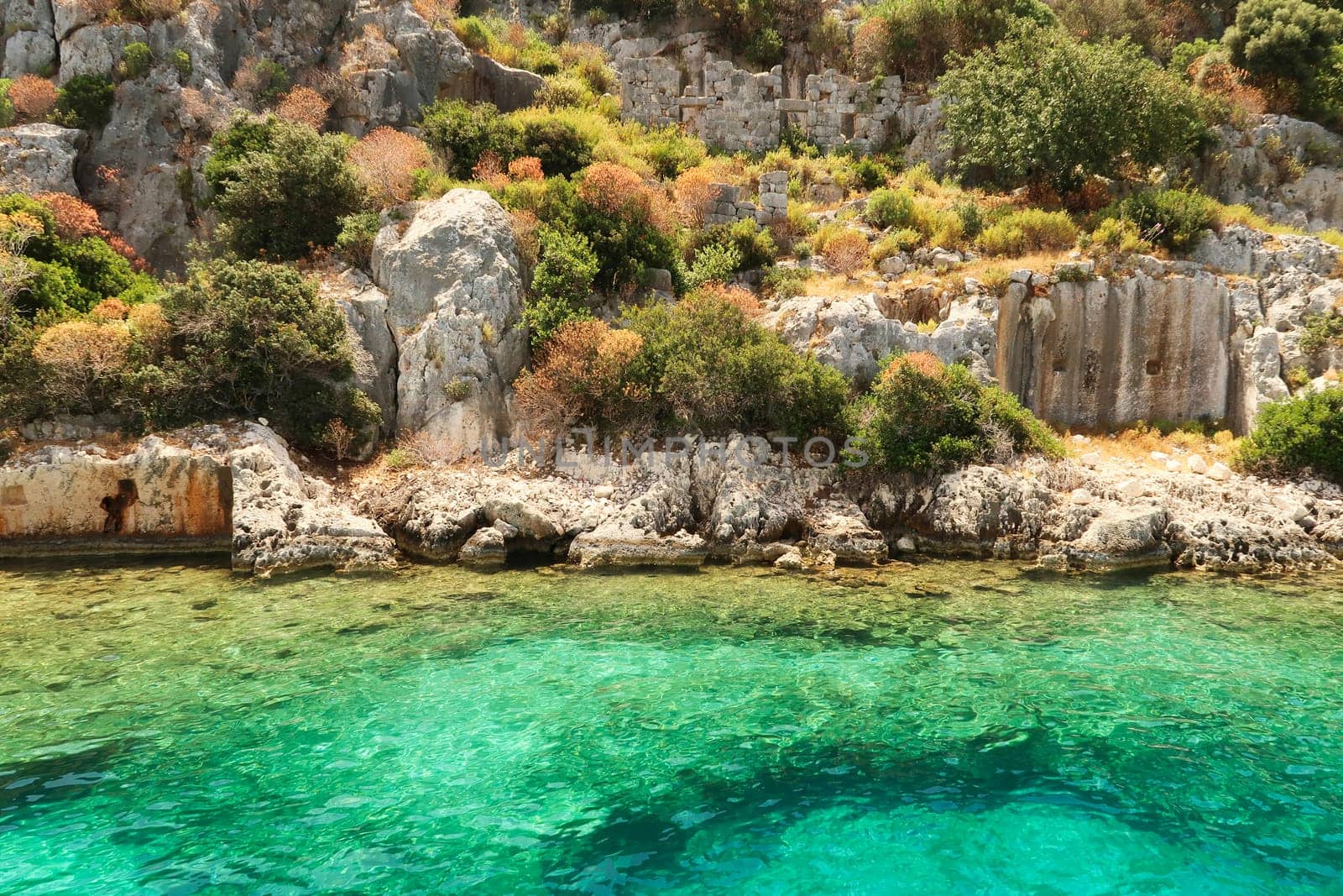 Submerged foundation in the foreground and structures and wall with window and doors onshore in the background at the ancient sunken city of Kekova, Kekova Island, Demre, Turkey 2022