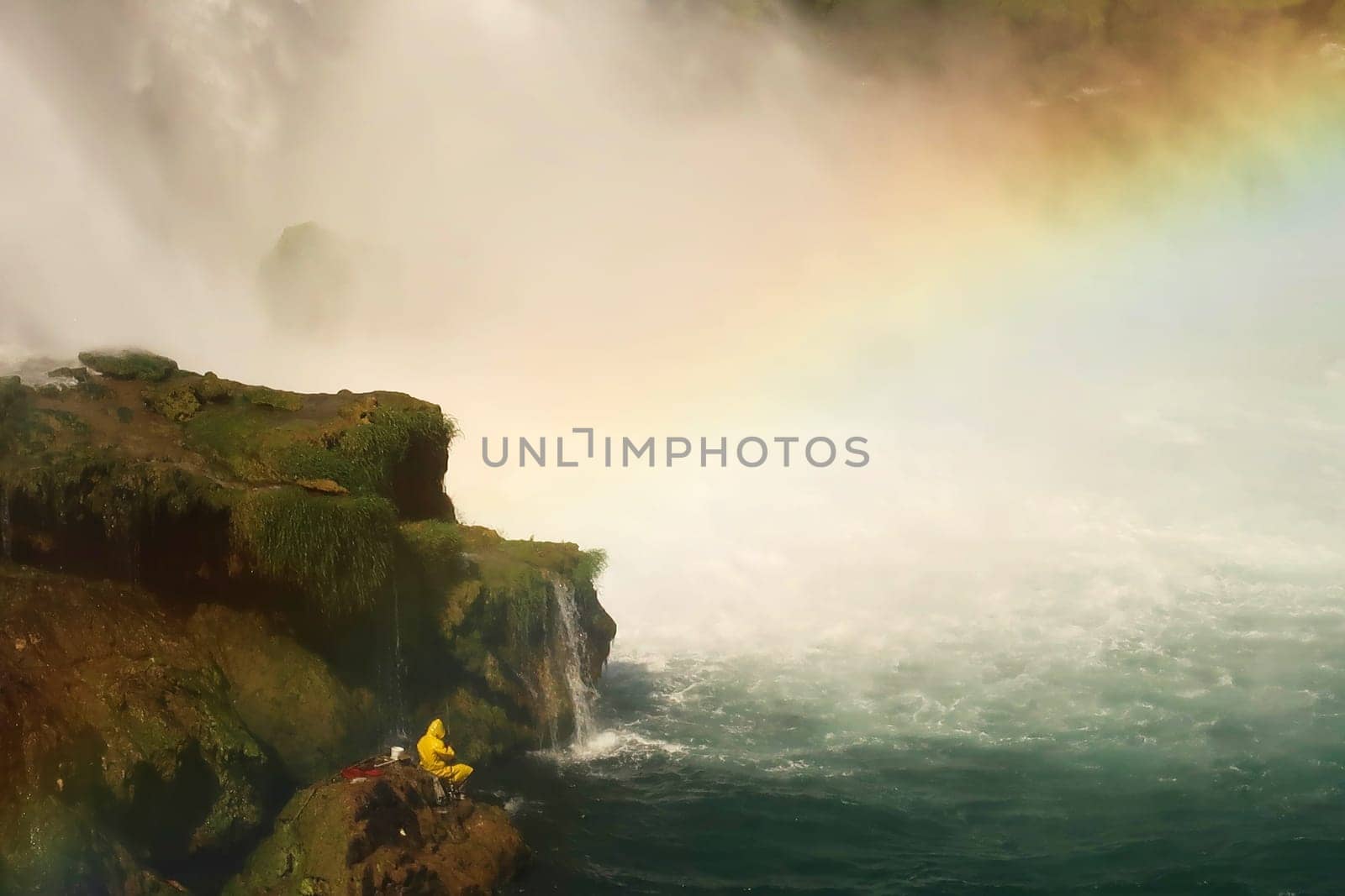 Fisherman in bright yellow raincoat fishing from a rock right next to the Düden Waterfalls in Antalya, Turkey 2022