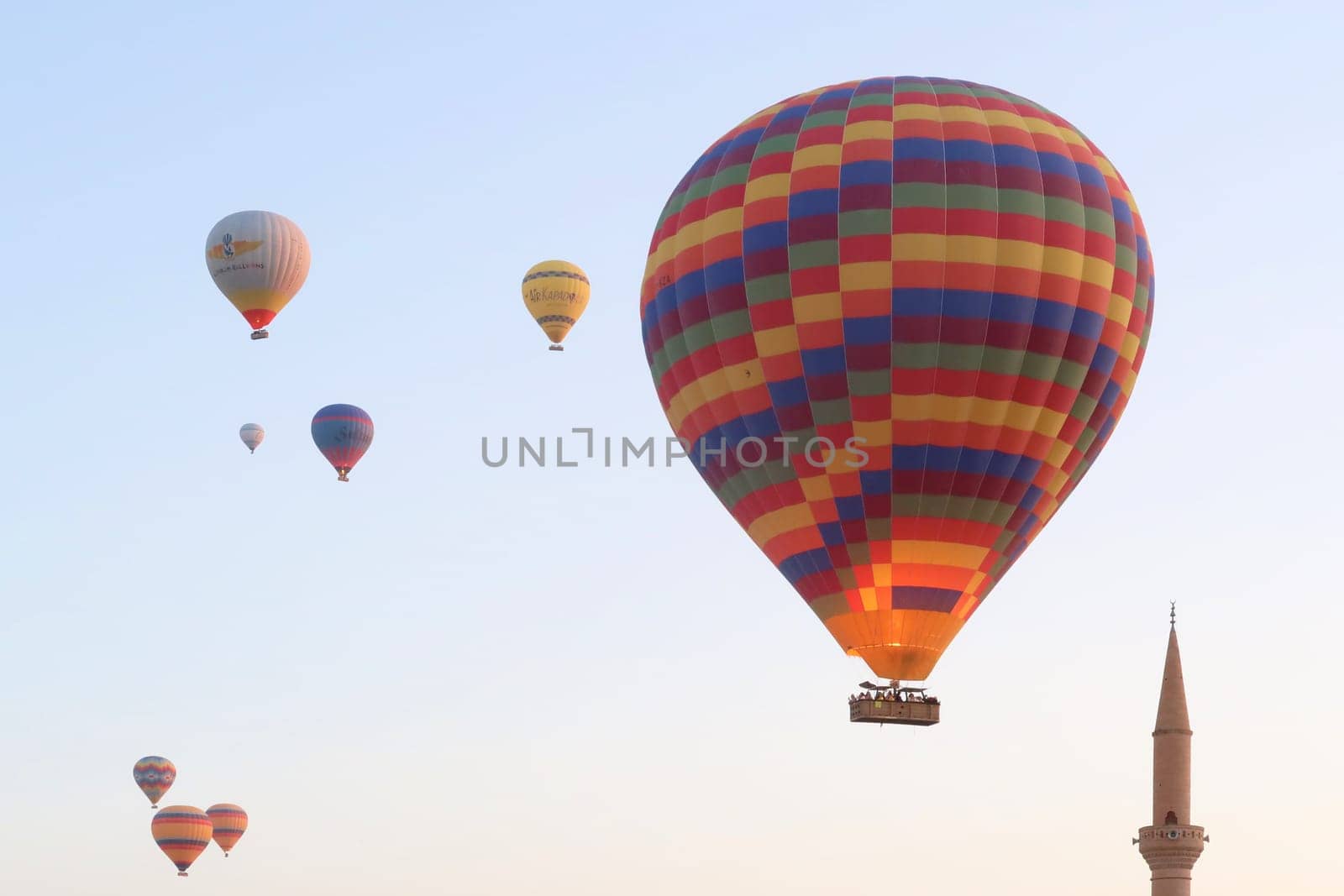 Colorful group of air balloons in the early morning over the town of Göreme with the tower of a Minaret right next to it, Göreme, Cappadocia, Turkey 2022