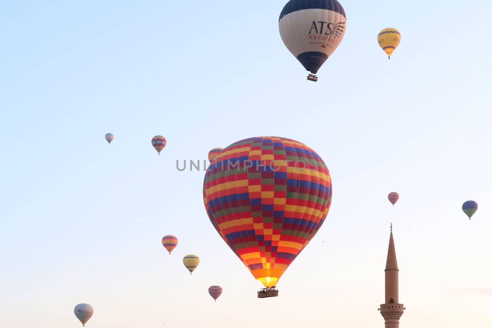 Hot air balloons in the early morning over the town of Göreme with the tower of a Minaret right next to it, Göreme, Cappadocia, Turkey 2022