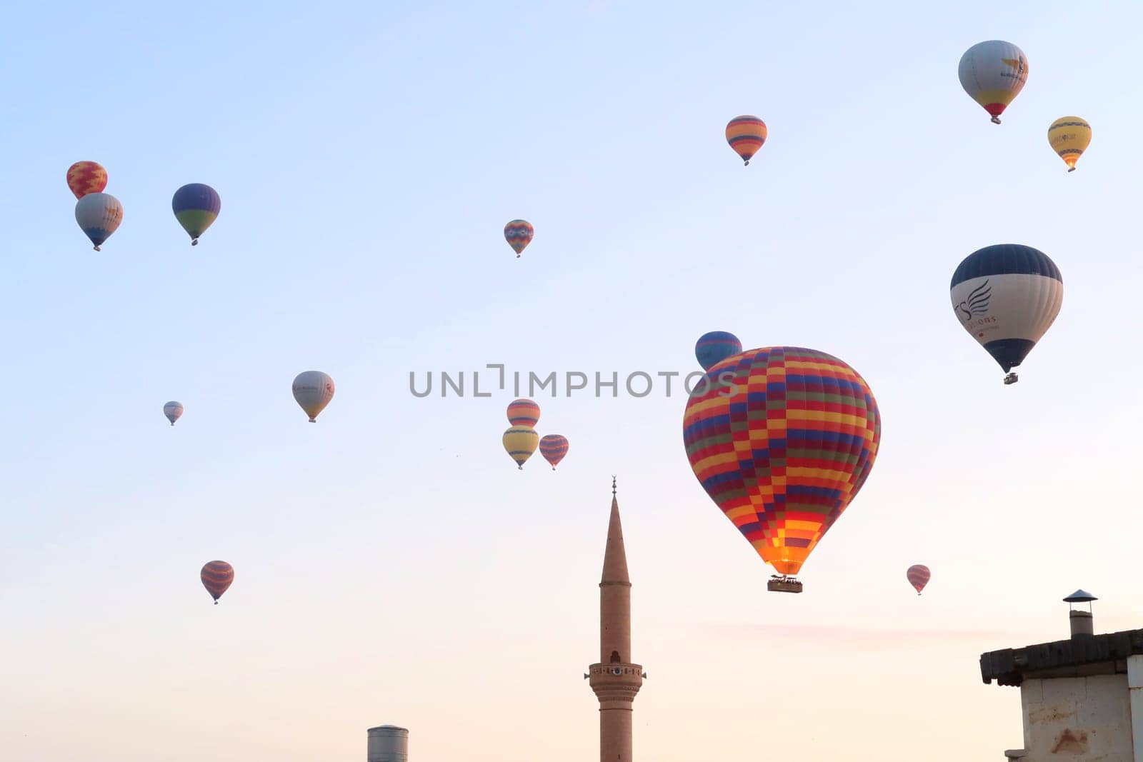 Colorful hot air balloons in the early morning over the town of Göreme with the tower of a Minaret right next to it, Göreme, Cappadocia, Turkey 2022