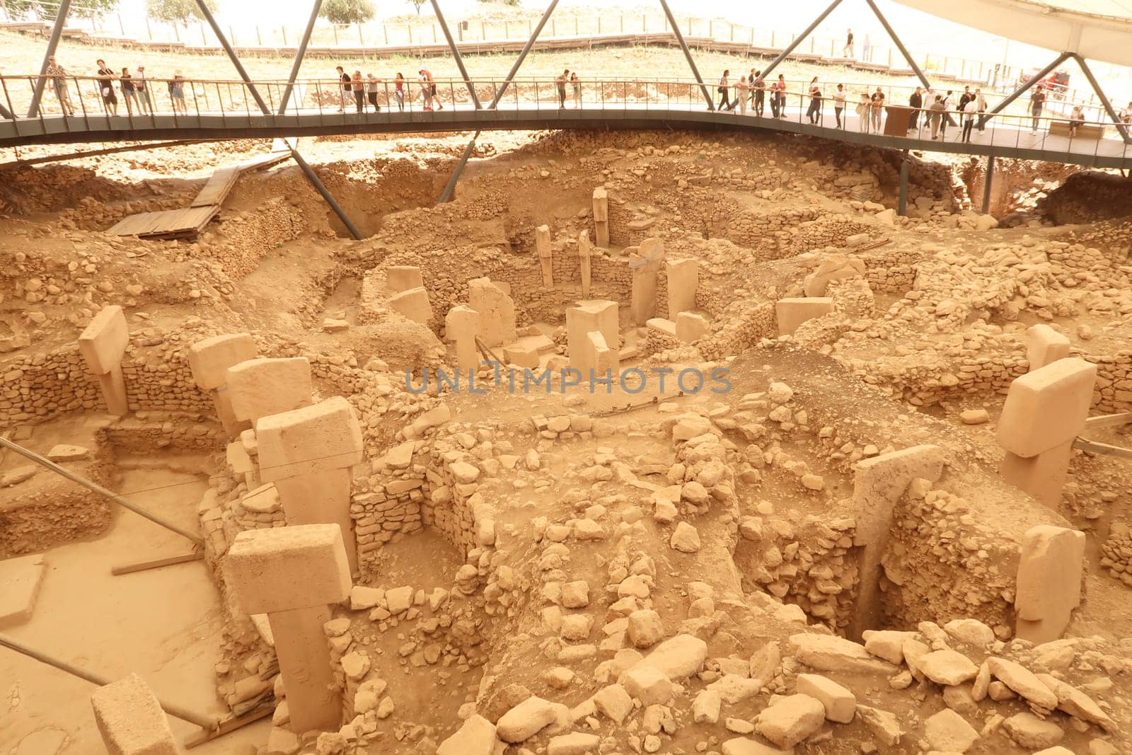 The main enclosures at the neolithic archaelogical site of Göbekli Tepe, the wooden walkway going around it with visitors on it can be seen in the background, Göbekli Tepe, Sanliurfa, Turkey, 12th of June 2022