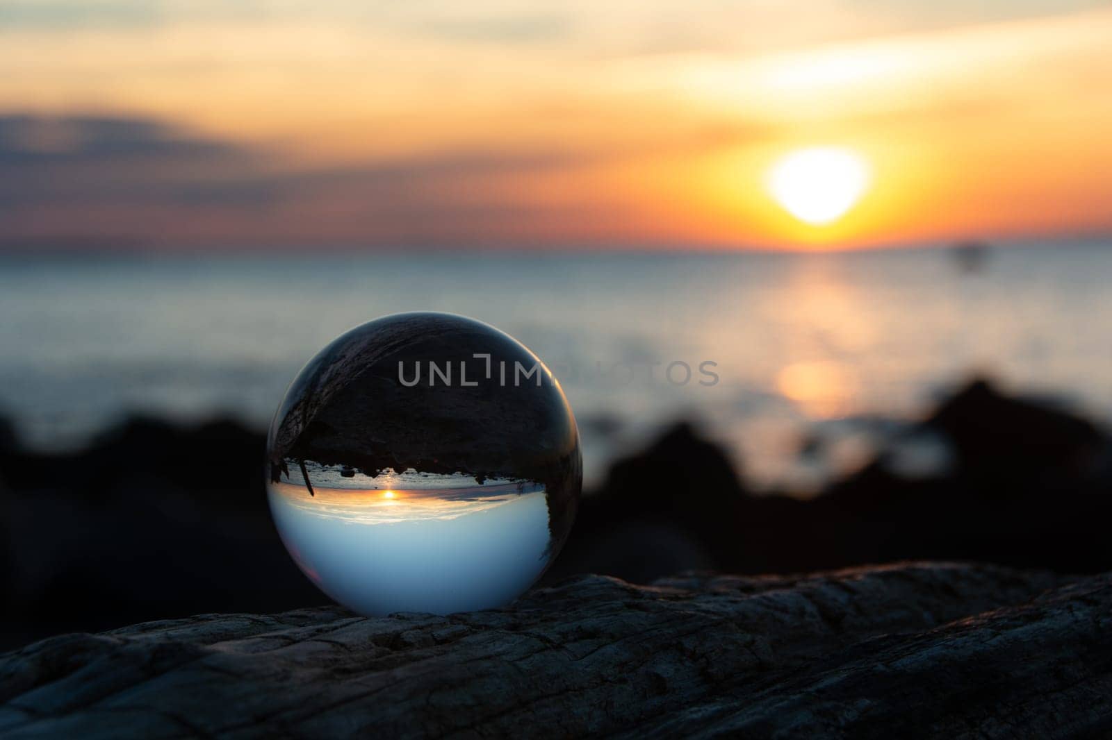 Glass ball on a branch at sunset on the beach, the sea and the setting sun are reflected in the ball