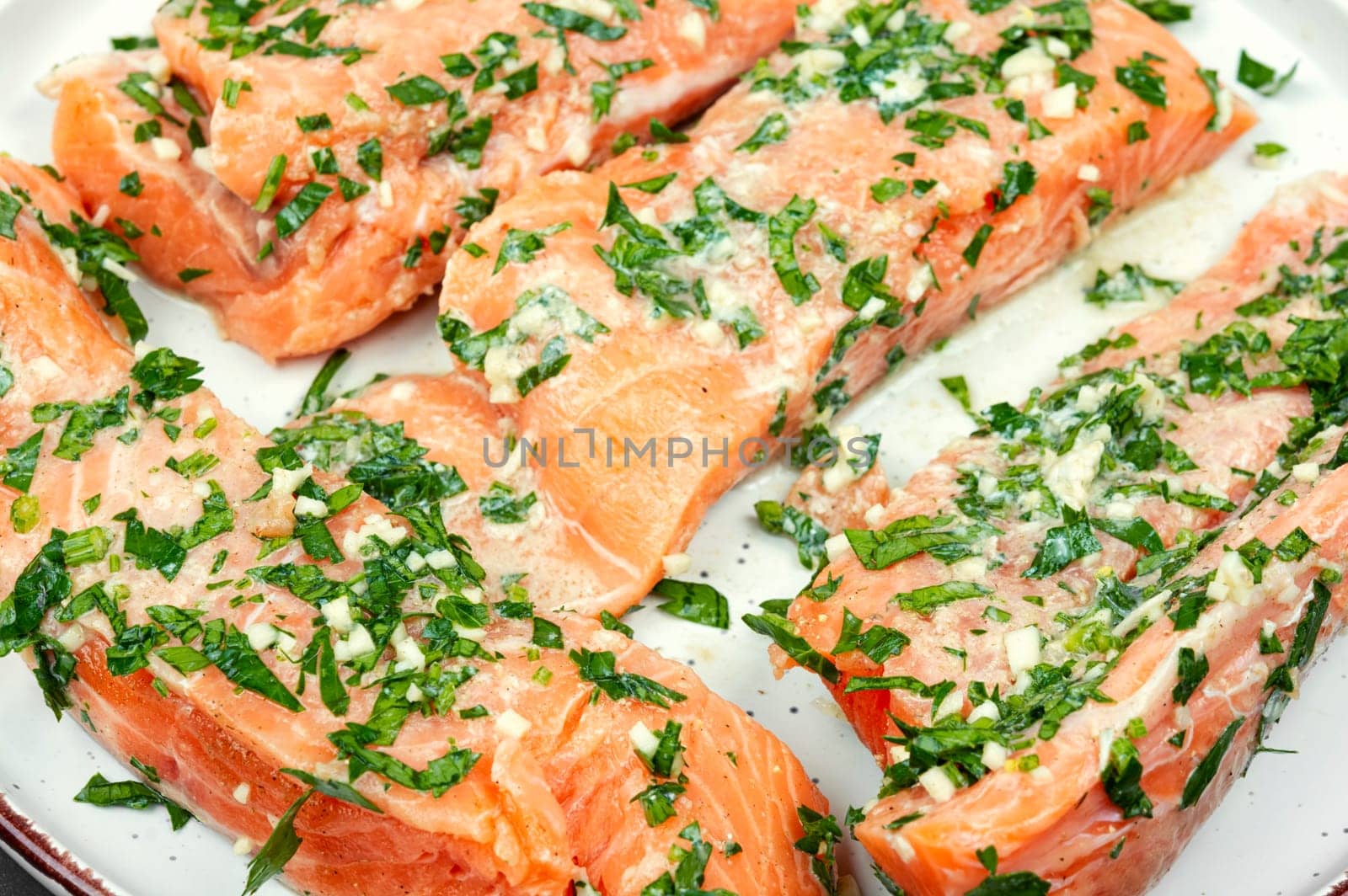 Fresh raw salmon fillet fish in garlic herbs marinade ready for baking. Close up.