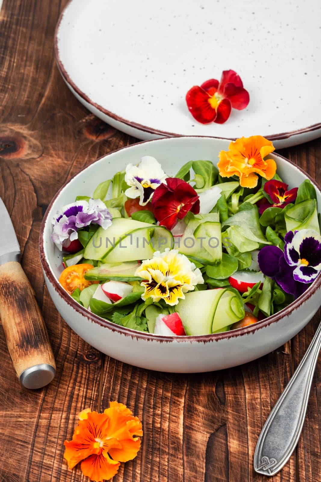 Healthy salad made from fresh vegetables and decorated with edible flowers on rustic wooden table.