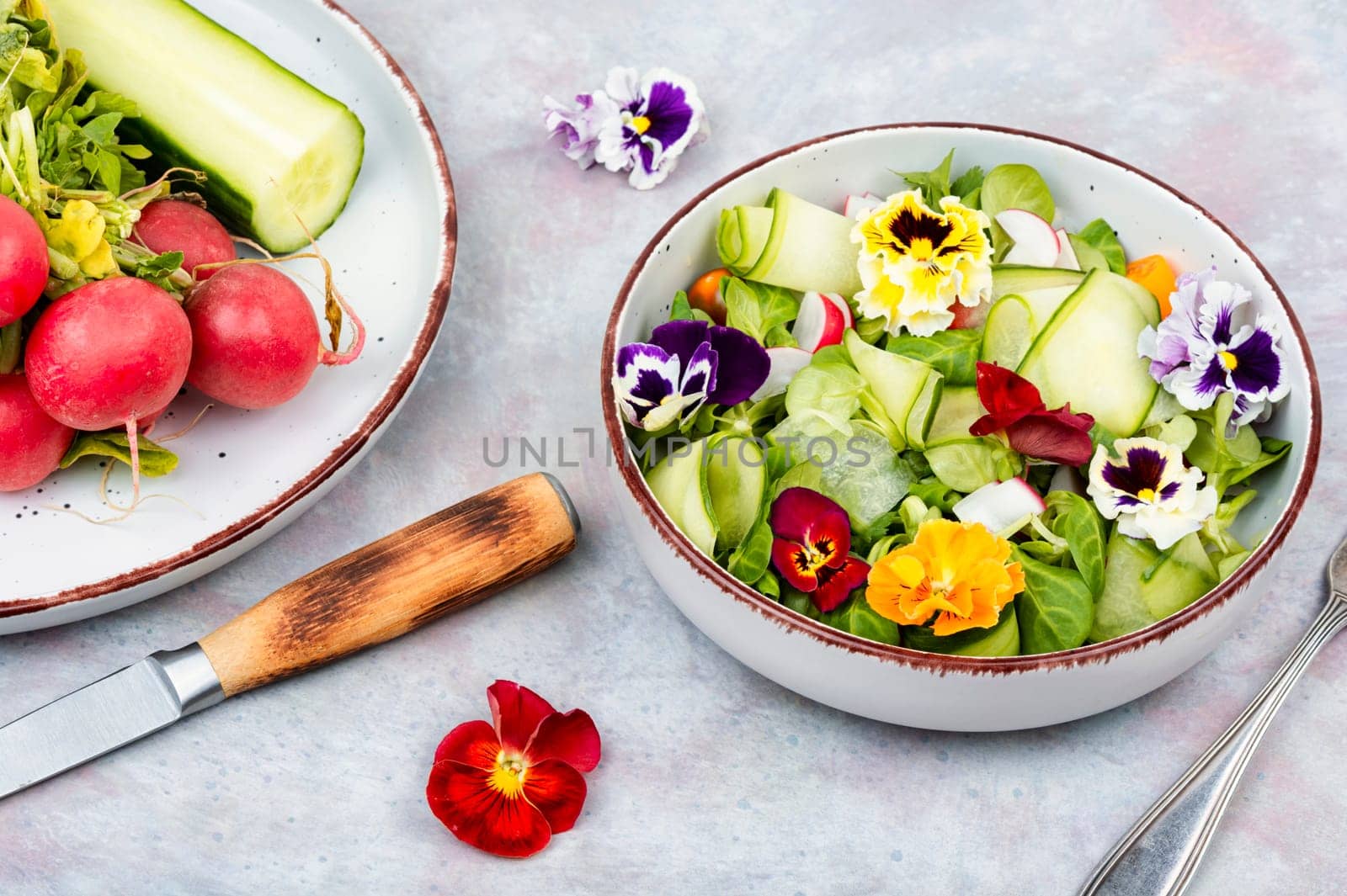 Healthy salad made from fresh vegetables and decorated with edible flowers on rustic wooden table.
