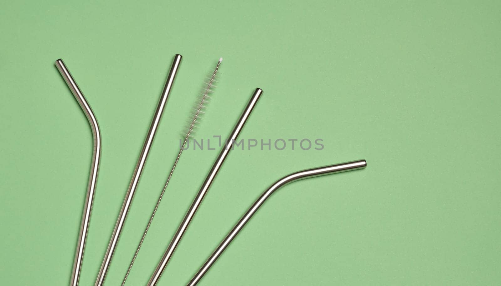 Metal straws for cocktails and a cleaning brush on a green background, top view