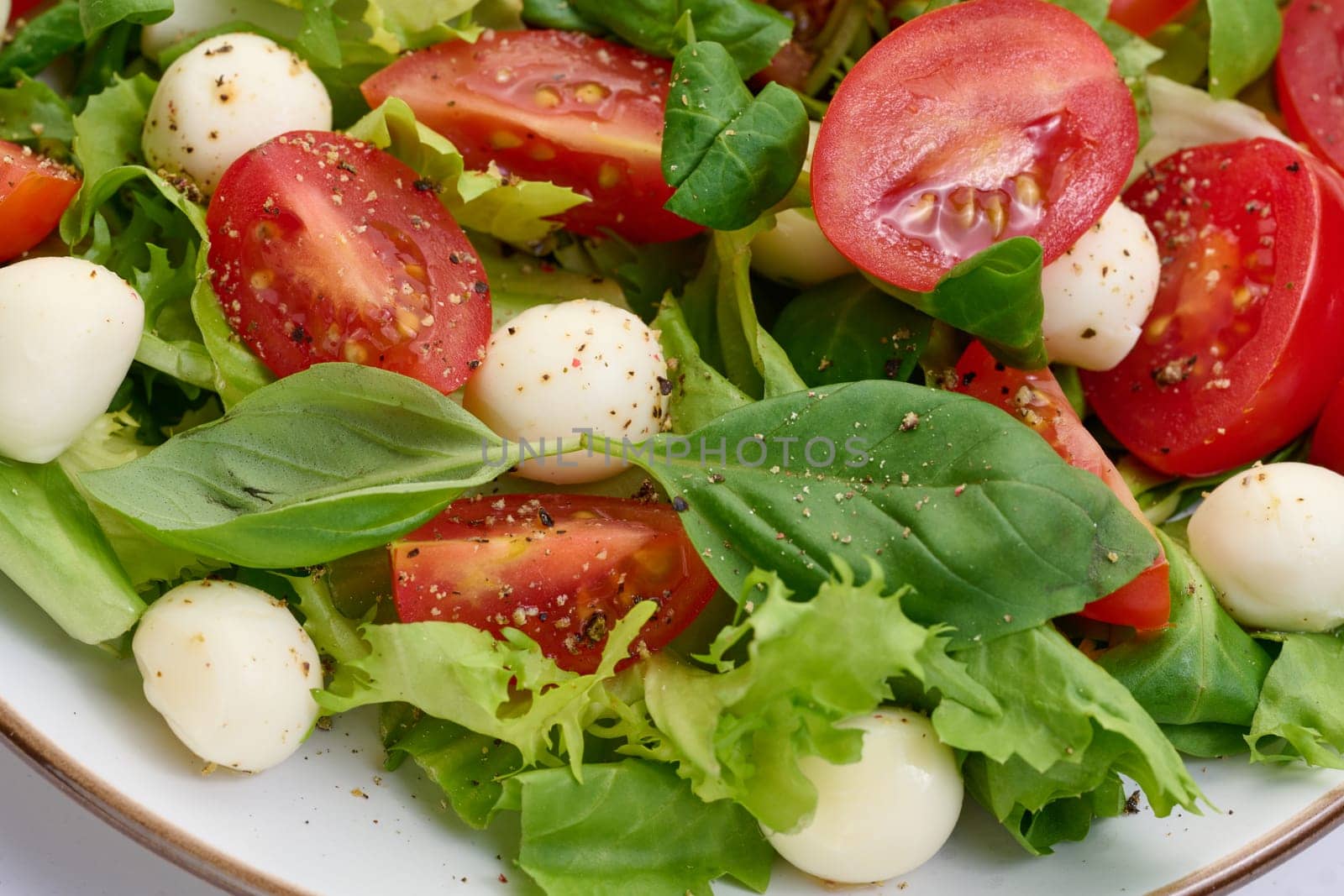 Salad with mozzarella, cherry tomatoes and green lettuce in a white round plate, close up