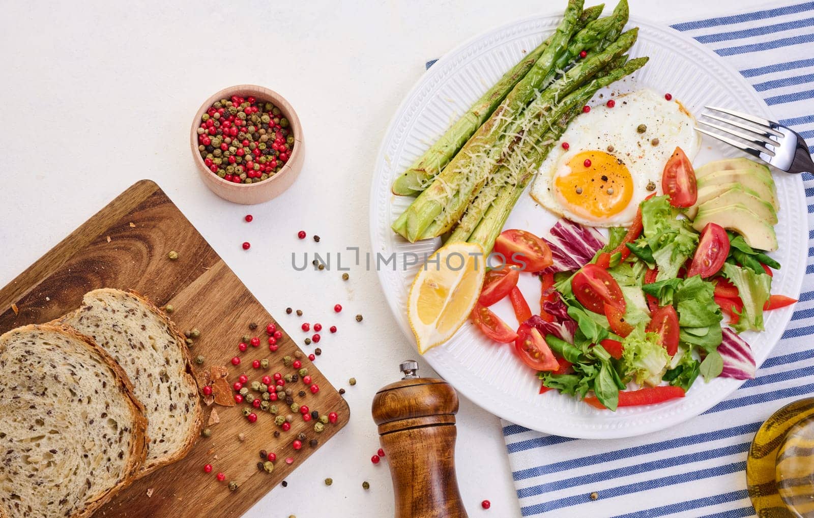 Round plate with cooked asparagus, fried egg, avocado and fresh vegetable salad on the table, top view