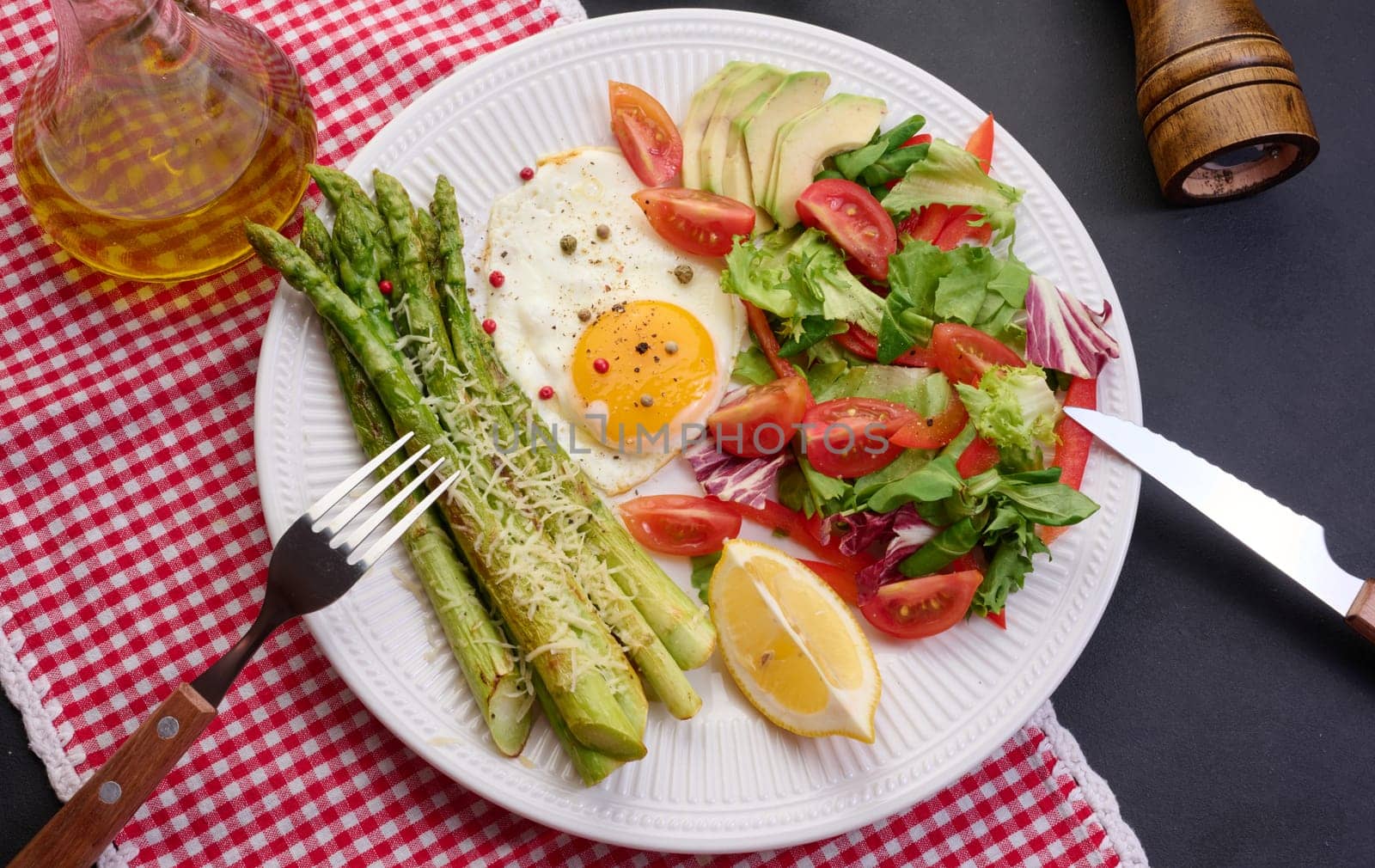 Round plate with cooked asparagus, fried egg, avocado and fresh vegetable salad on the table, top view